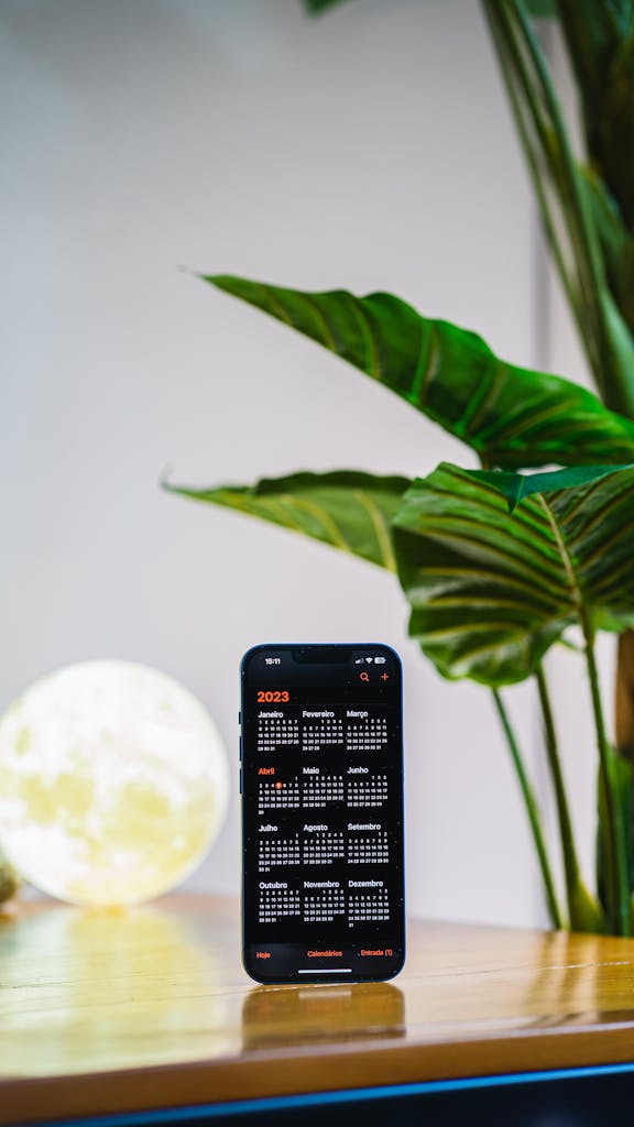 Smartphone showing 2023 calendar app on wooden table with plants.