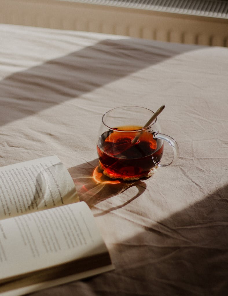 A glass of tea and an open book on a sunlit bed offer a cozy morning vibe.